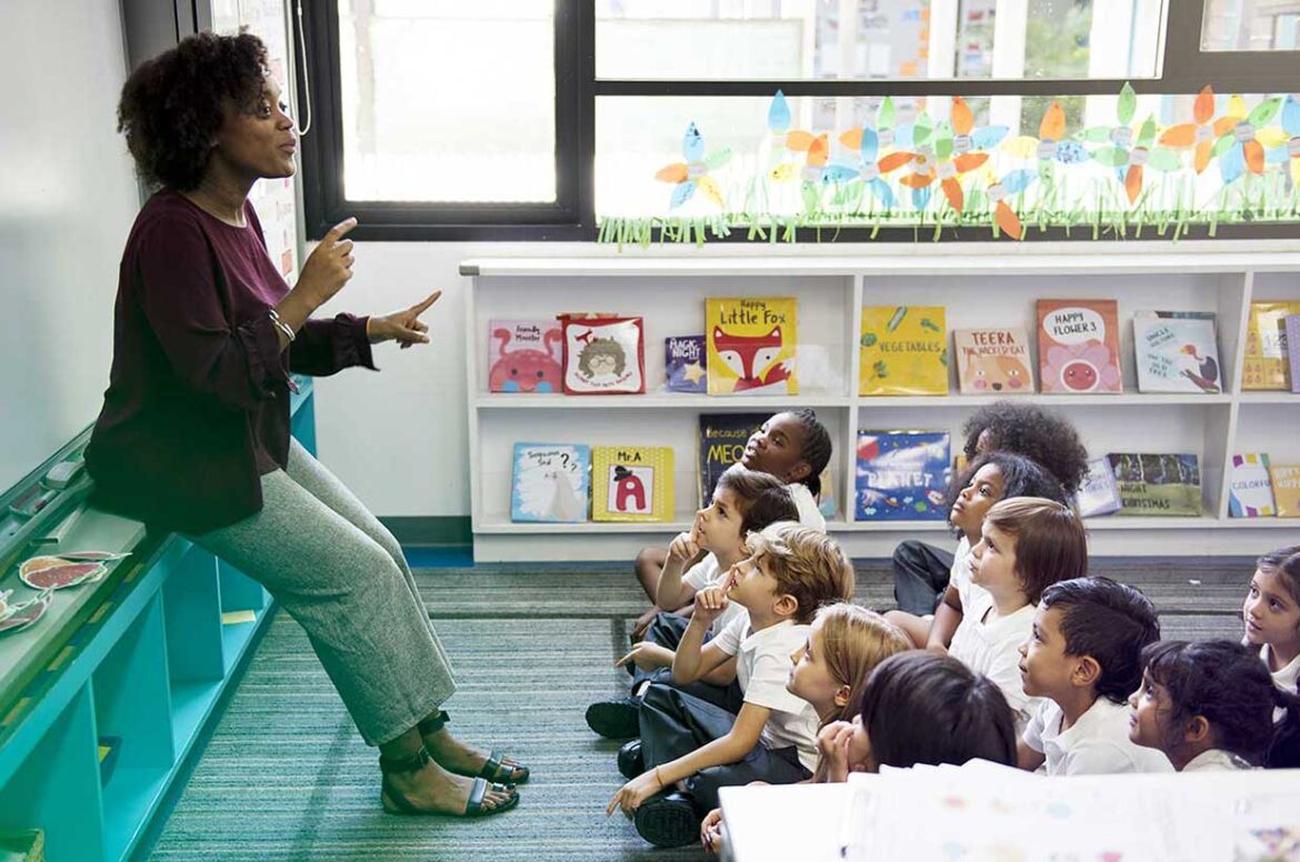 A female teacher teaching her students as they sit on a rug at her educational services center