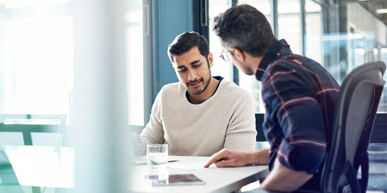 Two male small business owners sitting at a table together determining how to increase revenue.