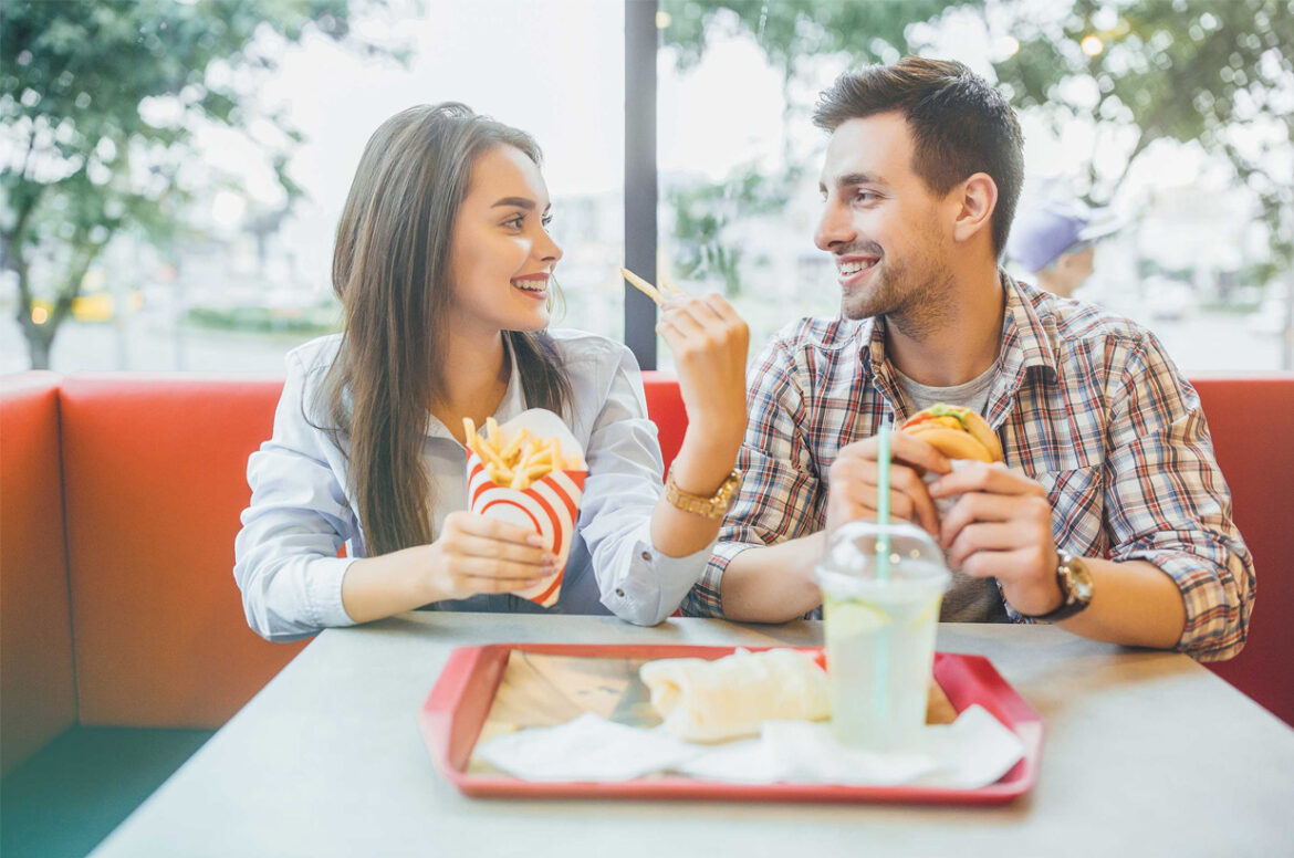 Two franchise restaurant owners are eating french fries and a burger at their restaurant.