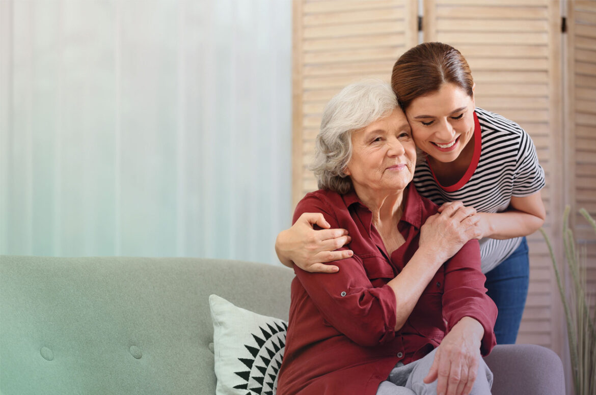 A female funeral home business owner is hugging a client that is sitting on a couch.
