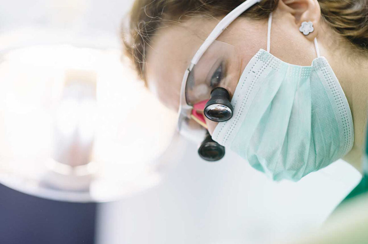 A female healthcare practice business owner is wearing a mask and glasses to perform medical care.