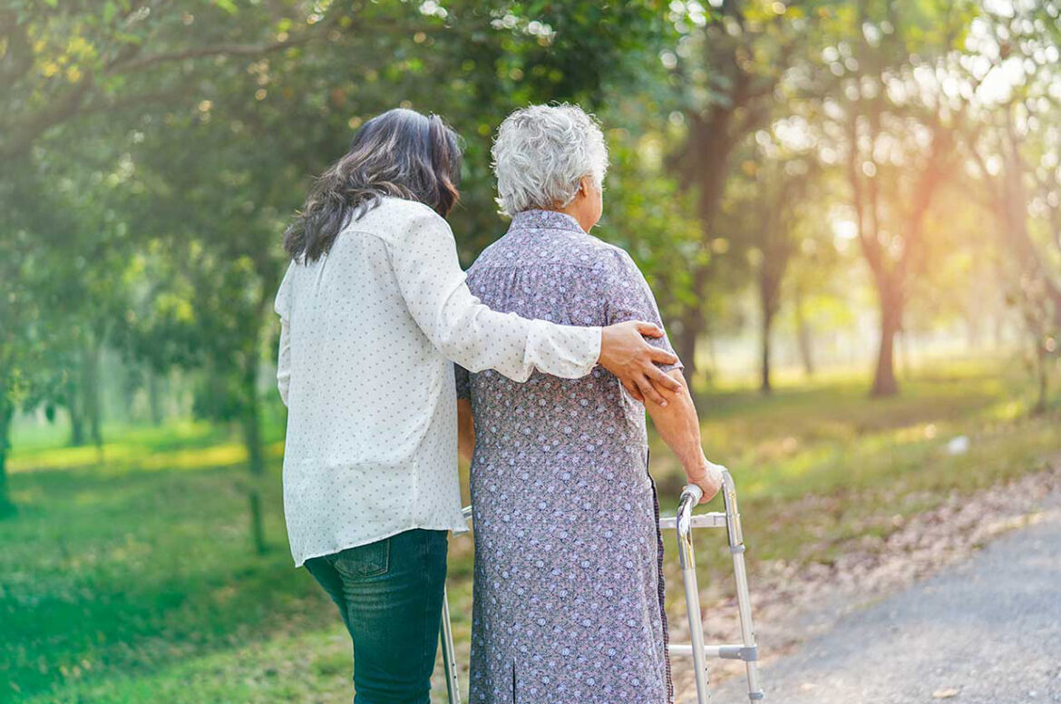 A female home care business owner is assisting a client who is using a walker.