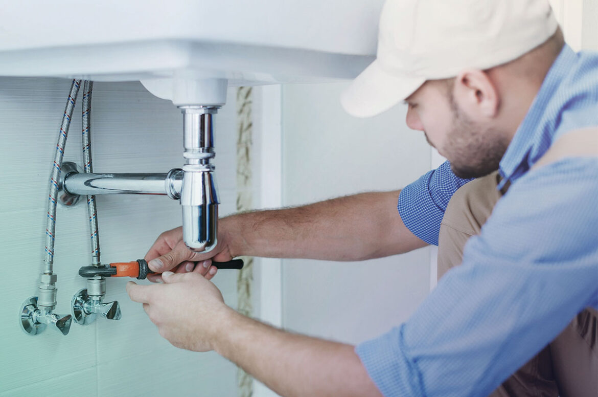 A male HVAC and plumbing contractor business owner is fixing a bathroom sink with a tool.