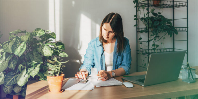 Female business owner sitting at a table calculating the cash flow for her small business.