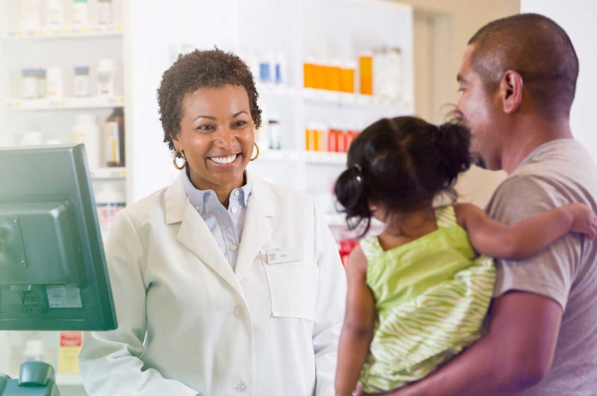 A pharmacy business owner is standing with a father and his daughter at a pharmacy.