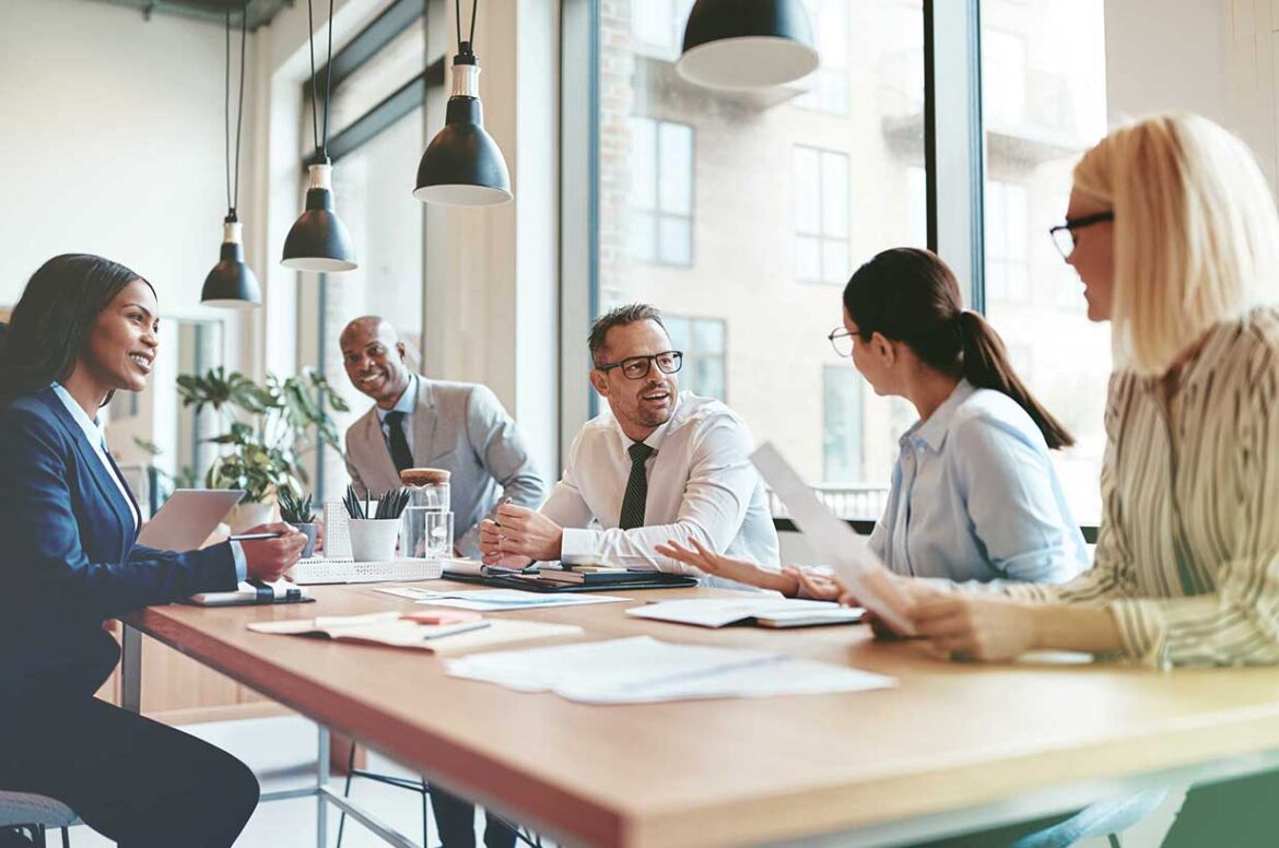 A male business owner meeting at a table with four employees to discuss their sponsor financing options