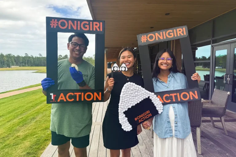 Three members of Live Oak Bank's Asian American Pacific Islander Community (AAPIC) employee resource pose for a group photo with props to support the Onigiri Action Table for Two event